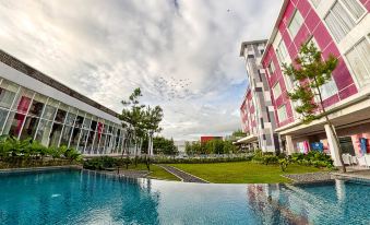 a modern , white - red - brick building with a glass facade , surrounded by green grass and trees , and a swimming pool in the foreground at Favehotel Cimanuk Garut