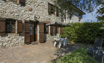 a stone house with wooden shutters , surrounded by trees and a patio with chairs and tables at Girasole