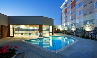 a large swimming pool with a building in the background and lights on , creating a serene atmosphere at Four Points by Sheraton Saginaw