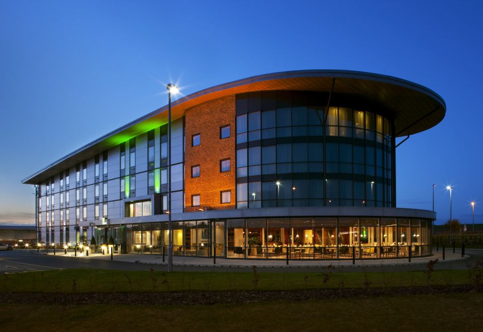 a modern building with a curved glass facade is lit up at night , and a green light shining on the entrance at Holiday Inn Salisbury - Stonehenge