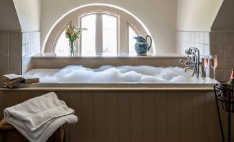 a bathtub filled with bubbles , a pitcher of water , and a vase of flowers on the windowsill at Chilston Park Hotel
