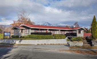 a large house with a red roof is surrounded by trees and mountains in the background at Arrowtown Motel