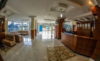 a hotel lobby with a reception desk , couches , and clocks , as well as a view of the outside through large windows at Fatima Hotel