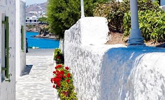 a white stone building with a staircase leading to the ocean , surrounded by colorful flowers at Mykonos Beach Hotel