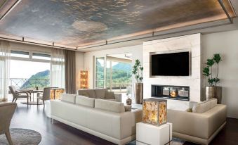 a spacious living room with white couches , chairs , and a large flat - screen tv mounted on the wall at Lefay Resort & Spa Lago di Garda