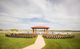 a wedding ceremony taking place outdoors , with chairs arranged for guests and a gazebo in the background at Arrowwood Resort at Cedar Shore