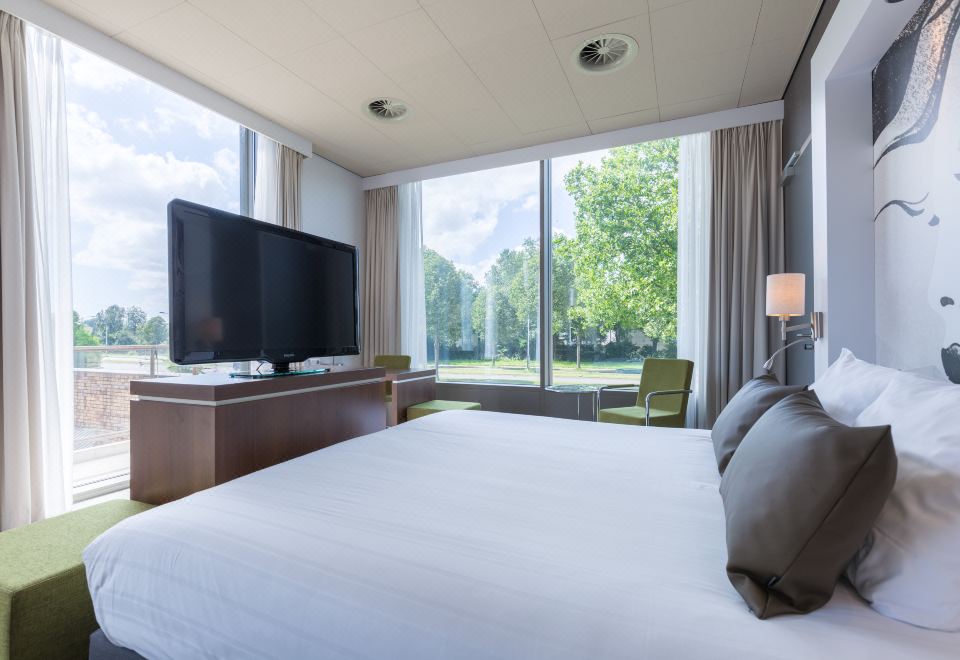 a large bed with a white comforter is in a room with a flat screen tv and a window at Leonardo Hotel Papendrecht