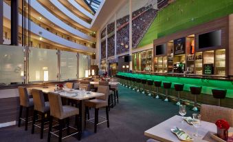 a modern restaurant with large windows , marble tables , and green seating areas , as well as a bar area with tables and chairs at Lindner Hotel Leverkusen Bayarena