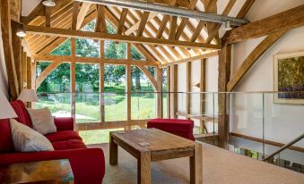 a room with wooden beams , large windows , and red chairs surrounding a table in front of a window at South Park Farm Barn