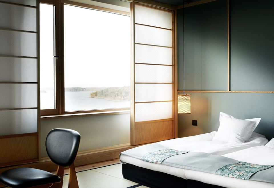 a modern bedroom with a large window , wooden blinds , and a bed with white linens at Yasuragi