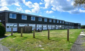 a long row of houses with wooden fences in front and blue skies overhead , next to a grassy field at North Devon Resort