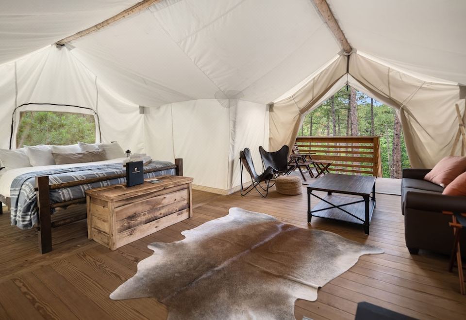 a cozy tent interior with a wooden floor , large windows , and a bed , as well as a black coffee table and chair at Under Canvas Mount Rushmore