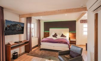 a modern bedroom with a large bed , leather chair , and a flat screen tv on the wall at Hotel Restaurant der Engel, Sasbachwalden