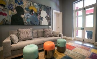 a living room with a gray couch , multiple orange and green ottomans , and a large painting on the wall at Ruby Rose