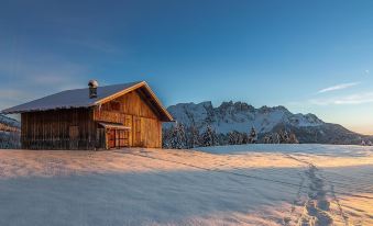 a wooden cabin is situated on a snow - covered hillside with mountains in the background , under a clear blue sky at Hotel Adler