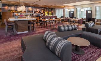 a modern lounge area with gray and black striped couches , tables , and a bar in the background at Courtyard by Marriott Fairfax Fair Oaks