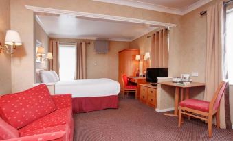 a hotel room with a red couch , white bed , and desk , along with other furniture at Garden Court Hotel Aylesbury