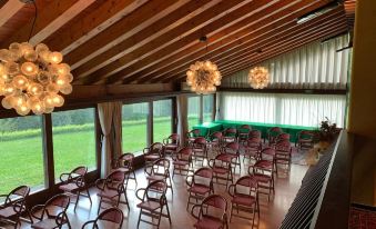 a room with wooden ceiling and walls , large windows , and several rows of chairs arranged in front of a green field at Hotel Bellavista