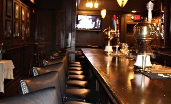 a dimly lit bar with a long wooden bar and several chairs , as well as a television mounted on the wall at Waynebrook Inn