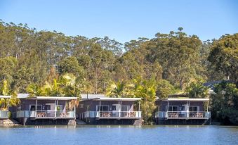 a row of small houses situated on stilts in the middle of a body of water , surrounded by trees at Ingenia Holidays Lake Conjola