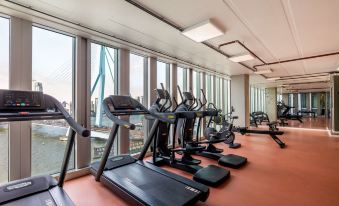 a gym with treadmills and other exercise equipment in front of large windows overlooking the city at Nhow Rotterdam