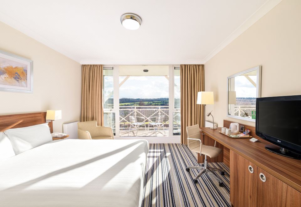 a hotel room with a comfortable bed , a desk , and a balcony overlooking the city at Holiday Inn Leeds - Brighouse