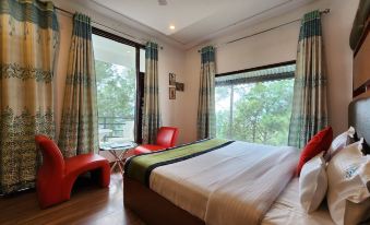 a spacious bedroom with a large bed , two red chairs , and a window overlooking trees at Hotel Bliss