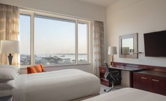 a modern hotel room with large windows offering views of the city , white bedding and furniture , and an orange desk area at Guyana Marriott Hotel Georgetown