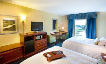 a hotel room with two beds , a desk , and a tv , all set against a backdrop of windows and a balcony at Hampton Inn & Suites Lake Wales
