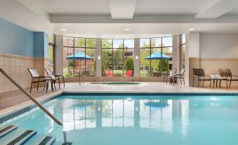 an indoor swimming pool surrounded by chairs and tables , with a view of the outdoors at Hilton Garden Inn Stony Brook