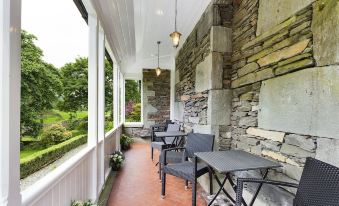 a porch with a brick wall and stone wall , featuring several chairs and a dining table at Crow How Country Guest House