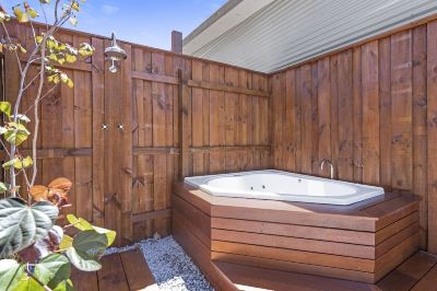 a wooden outdoor shower with a white bathtub and a palm tree nearby , under a clear blue sky at The Swan Valley Retreat