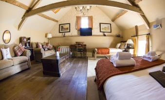 a spacious bedroom with a sloped ceiling and wooden floors , featuring a large bed , couch , and dining table at The Crown at Marnhull
