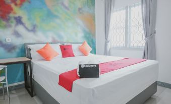 a large bed with white sheets and a red blanket is in a room with a colorful wall at RedDoorz @ Beringin Jambi