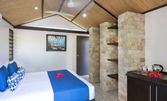 a cozy bedroom with a blue bedspread , stone walls , and a wooden ceiling , along with shelves and a plant at Mantaray Island Resort