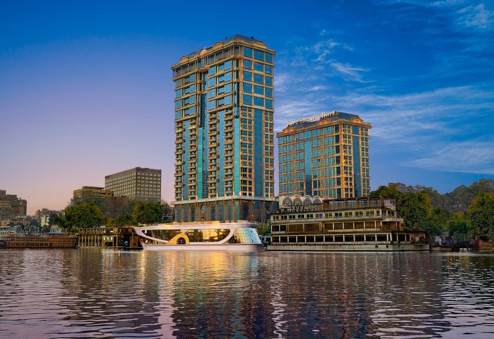 a large building with multiple floors and a unique design is reflected in the water at Four Seasons Hotel Cairo at the First Residence