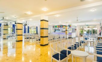 a large , well - lit room with yellow walls and floors , containing rows of white chairs arranged in a semicircle , possibly for an at Hotel Cala Murada