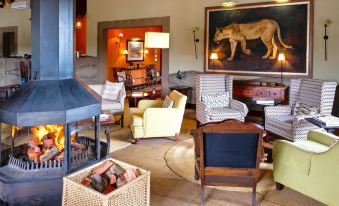 a cozy living room with a fireplace , chairs , and a painting on the wall , creating a warm and inviting atmosphere at Pumba Private Game Reserve