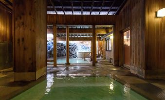 a wooden building with a large green pool in the middle , surrounded by trees and mountains at Naraya