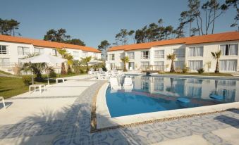 a large swimming pool is surrounded by a patio and white buildings with red roofs at Punta del Este Arenas Hotel