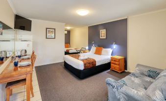 a modern hotel room with a large bed , two nightstands , and a couch , all set against a gray carpet at Best Western Caboolture Gateway Motel