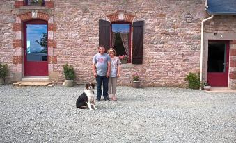 a man and a woman are standing next to a dog , posing for a picture in front of a stone building at La Clef des Champs