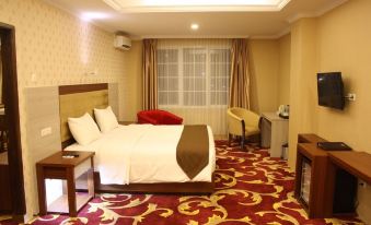 a hotel room with a bed , couch , and desk , all set against a red and gold patterned carpet at Grand Asrilia Hotel