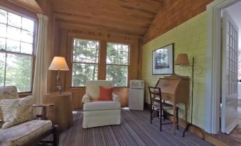 a cozy living room with wooden walls , large windows , and a comfortable chair , along with a desk and refrigerator at Harbourside Inn