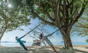 a man and a woman are practicing yoga under a large tree on a sandy beach at Island Escape Burasari
