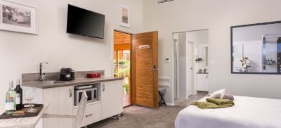 a modern living room with wooden doors , a tv on the wall , and a kitchenette at The Swan Valley Retreat