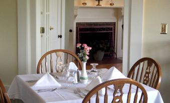 a dining table with a white tablecloth and wooden chairs is set in a room with a fireplace at Sunset Hill House