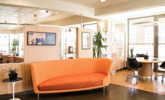 a modern office space with an orange couch in the center , surrounded by chairs and a desk at Ibis Como