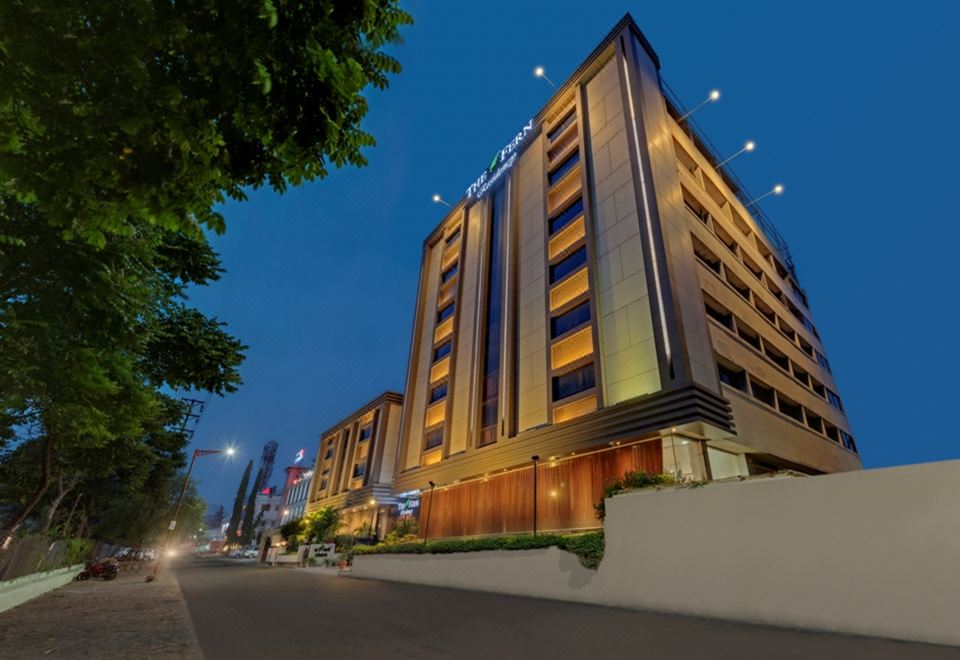 a modern hotel building with multiple floors , lit up at night , surrounded by trees and a street at The Fern Residency Aurangabad