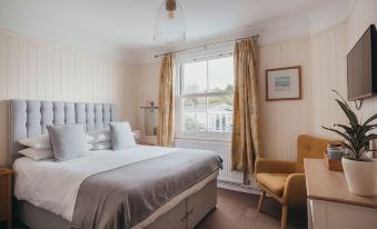 a well - decorated bedroom with a large bed , white walls , and a window looking out onto a sunny day at The Bay Hotel